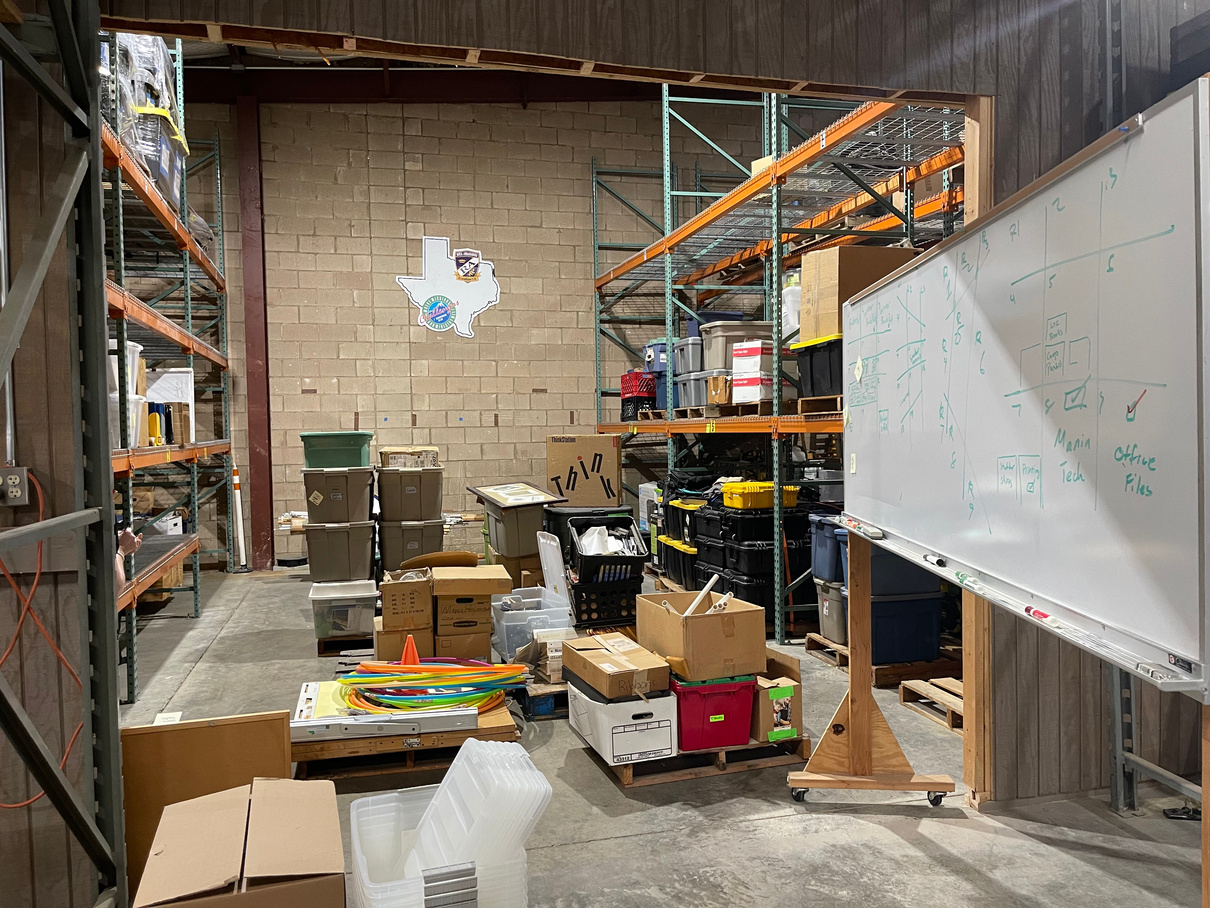 a cluttered warehouse with a whiteboard and lots of boxes